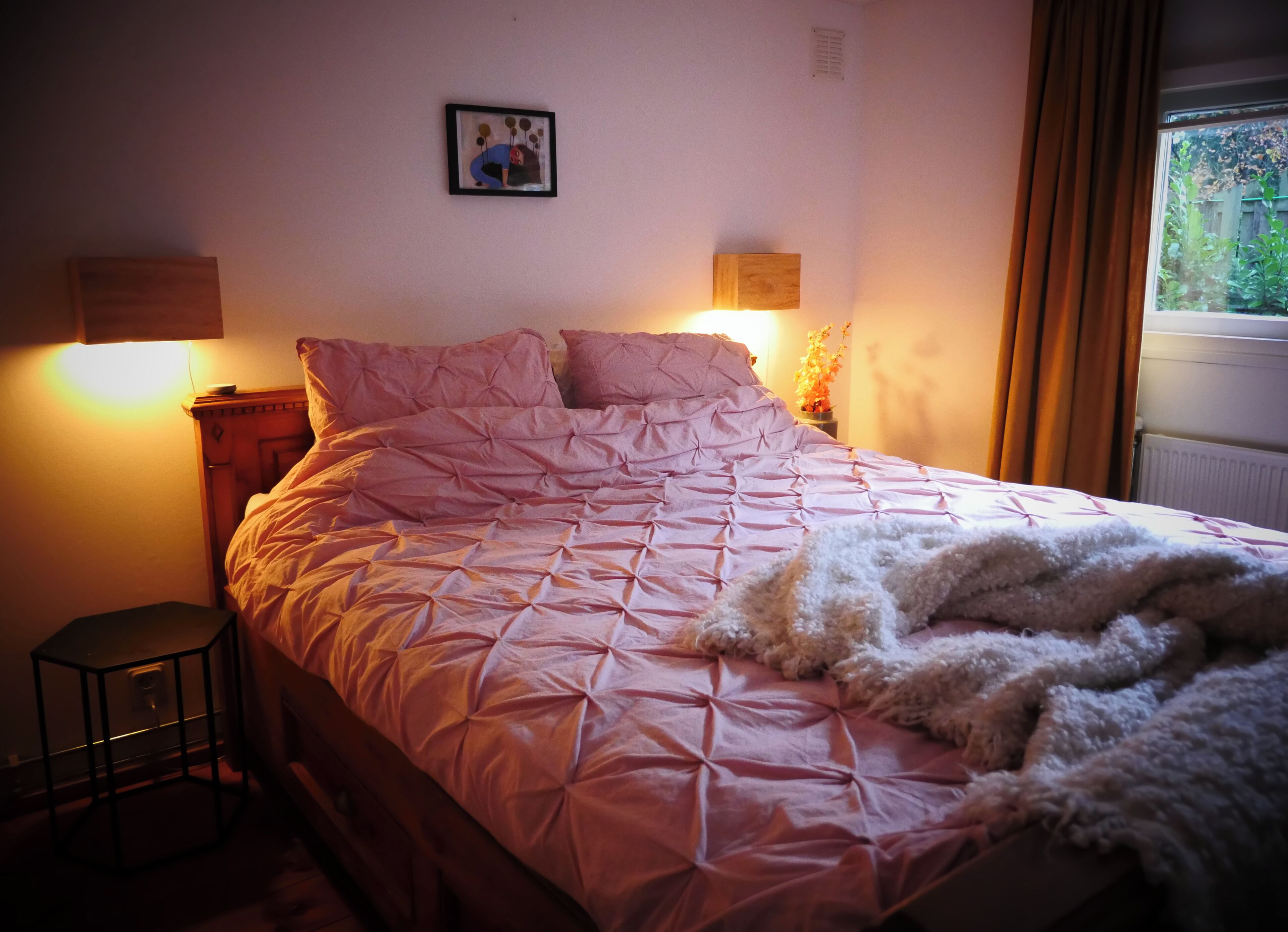 Un dormitorio con cama, lámparas de noche, un cuadro en la pared y una ventana con cortinas.