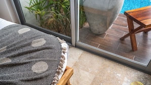 A room with a bed, a wooden stool, a woven mat, and a view of a pool through a glass door. - NHOA 101C 1BR Lux Pool access Aldea Zama (Tulum)