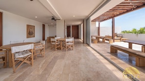 A spacious indoor area with wooden tables and benches, large windows, and a ceiling fan. - NHOA 101C 1BR Lux Pool access Aldea Zama (Tulum)