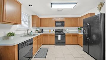 A modern kitchen with wooden cabinets, a black refrigerator, a microwave, a stove, and a dishwasher.
