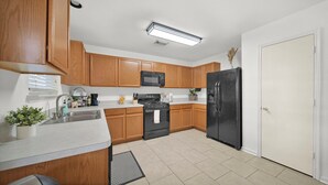 A modern kitchen with wooden cabinets, a black refrigerator, a microwave, and a stove. - Spacious 4-bedroom house with AC, hot tub, and WiFi in welcoming Tomball  (Tomball)
