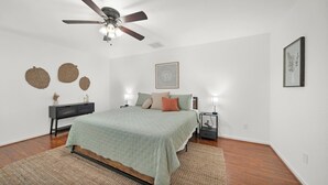 A bedroom with a bed, a ceiling fan, a nightstand, a lamp, and wall decorations. - Spacious 4-bedroom house with AC, hot tub, and WiFi in welcoming Tomball  (Tomball)