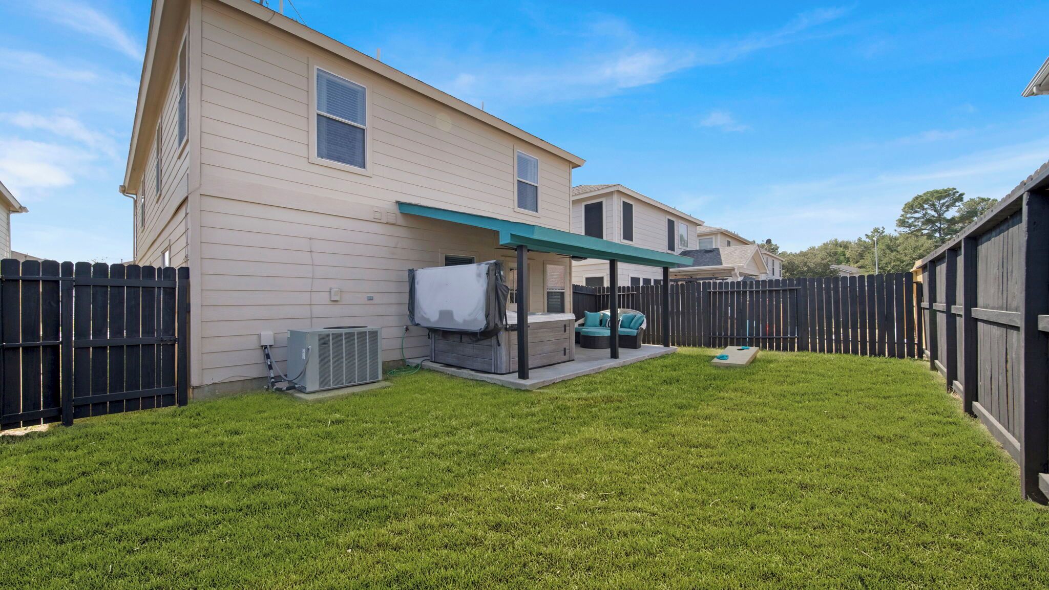 A residential backyard with a covered patio, a hot tub, and a fenced area.