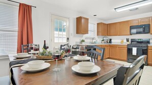 A modern kitchen with wooden cabinets, a microwave, an oven, and a dining table set with plates and wine glasses. - Spacious 4-bedroom house with AC, hot tub, and WiFi in welcoming Tomball  (Tomball)