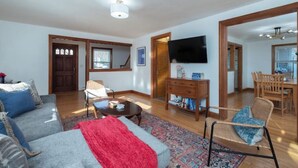 Una sala de estar con sofá, mesa de centro y televisor. Hay un comedor con una mesa y sillas.