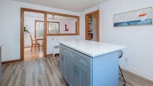 Una cocina moderna con encimera blanca, armarios azules y un marco de madera que da a un comedor.