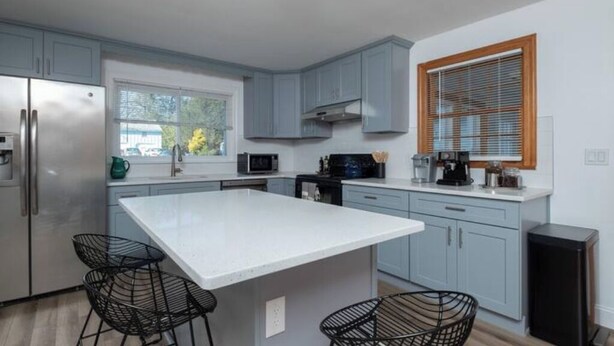 Una cocina moderna con gabinetes grises, una isla grande y sillas negras de metal.