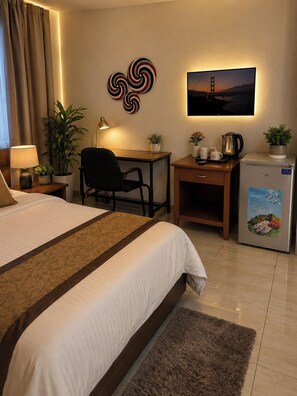 A hotel room with a bed, desk, chair, and a refrigerator.