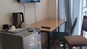 A compact room with a flat-screen TV mounted on the wall, a small refrigerator, a wooden desk, a chair, and a window with curtains. - Remarkable 3-Bed House in Kigali (Kigali)