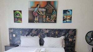 A hotel room with a bed, a headboard, a wall-mounted fan, and artwork on the wall. - Remarkable 3-Bed House in Kigali (Kigali)
