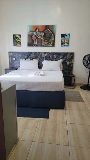 Ein Hotelzimmer mit Bett, Kopfteil, Wandventilator und einem Bild an der Wand.