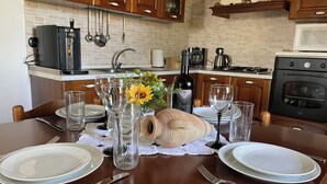 Una mesa de comedor lista con platos, cubiertos y copas de vino, con una hogaza de pan y un jarrón de flores sobre la mesa.