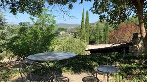 An outdoor seating area with two metal tables and chairs, surrounded by greenery and a stone structure. - Logis Hotel Le Clos Des Sullys (Montclus)
