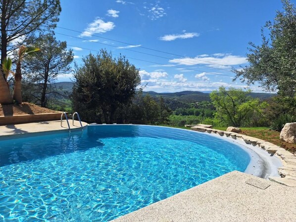 A clear blue swimming pool with a stone edge, surrounded by greenery and trees. - Logis Hotel Le Clos Des Sullys (Montclus)