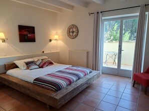 A bedroom with a wooden bed, a clock, a radiator, and a view of the outside. - Logis Hotel Le Clos Des Sullys (Montclus)