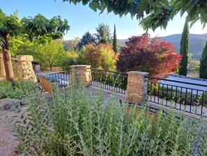 A stone pathway leading to a seating area with a metal railing, surrounded by lush greenery and trees. - Logis Hotel Le Clos Des Sullys (Montclus)