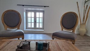 A room with two wooden chairs with grey cushions, a wooden table with a tray of candles, and a window with a view of the outside. - Logis Hotel Le Clos Des Sullys (Montclus)