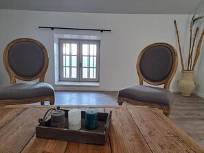 A room with two wooden chairs with grey cushions, a wooden table with a tray of candles, and a window with a view of the outside. - Logis Hotel Le Clos Des Sullys (Montclus)