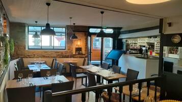 Un restaurante con varias mesas y sillas, una zona de bar y vistas a la calle.
