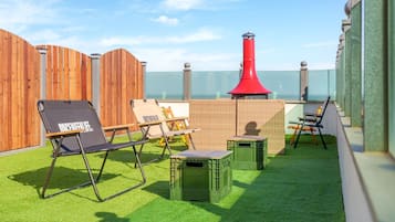 A rooftop terrace with a wooden fence, a red chimney, and outdoor seating.