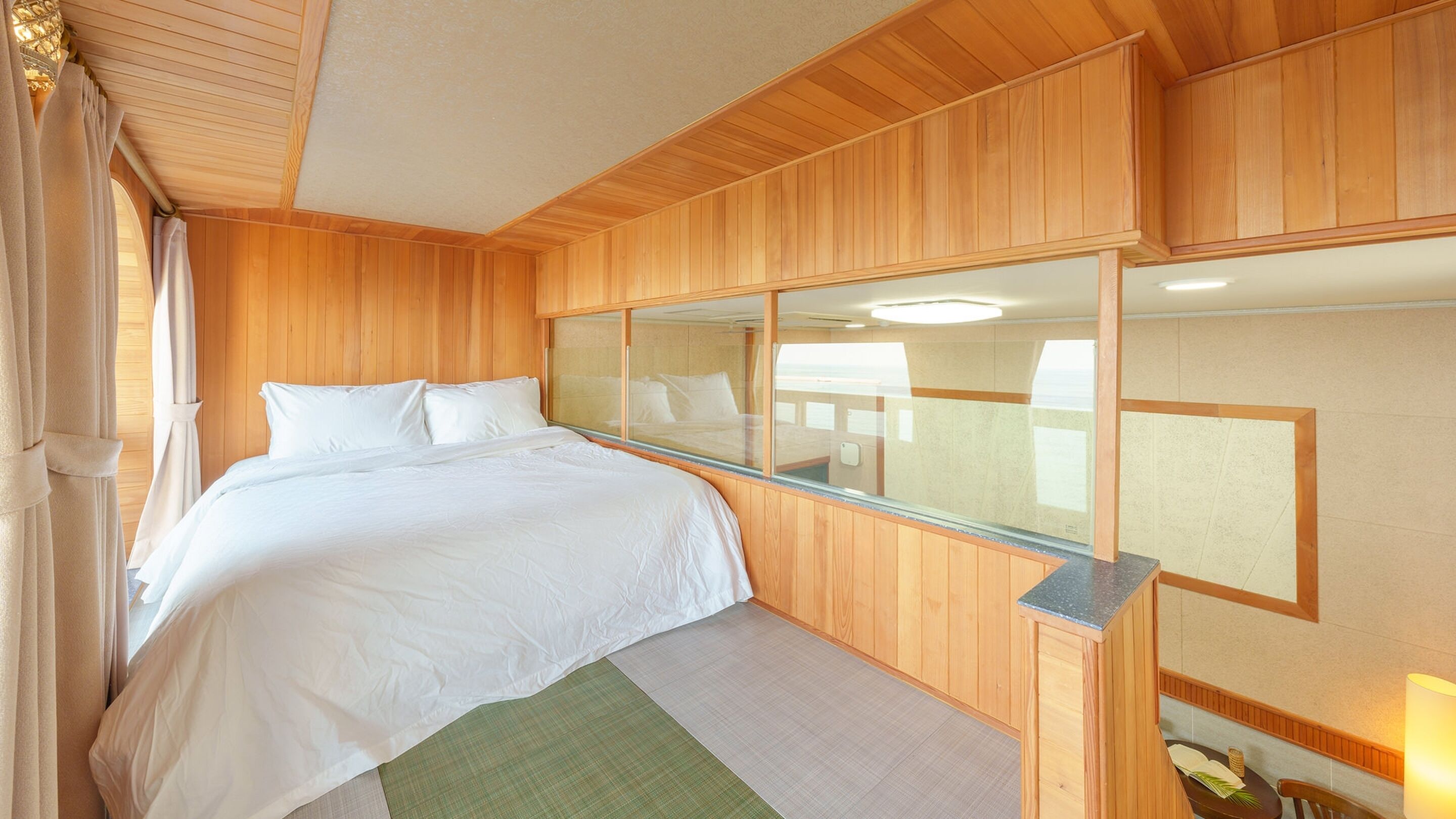 A wooden-paneled room with a bed, a large window, and a view of the sea.