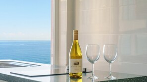 Una botella de Chardonnay Canyon Oaks 2022 y dos copas de vino vacías sobre una encimera con vista al océano.