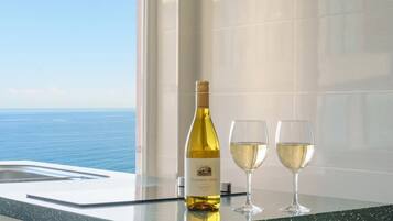 Una botella de Chardonnay Canyon Oaks 2022 y dos copas sobre una superficie reflectante, con vista al océano a través de una ventana.