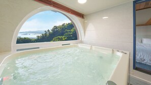 Un cuarto de spa con una bañera grande y vistas a un paisaje natural a través de una ventana semicircular.