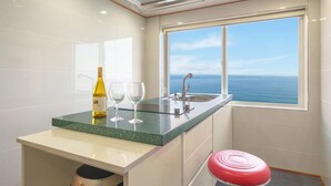 A kitchen with a green countertop, a wine bottle, two glasses, a sink, and a window with a view of the ocean. - Samcheok Peacehousing Spa Pet Pension (Samcheok)