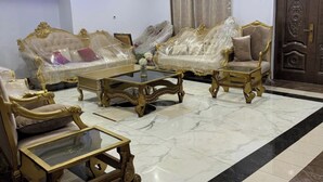 A room with a marble floor, two sofas with gold accents, a glass coffee table, and a wooden side table.