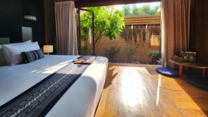 Ein Schlafzimmer mit einem großen Bett, einem kleinen Tisch und Blick auf Grünflächen.