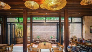 Ein Restaurant mit Holztischen, großen Fenstern und hängenden Lampen.
