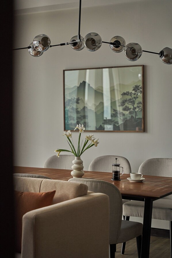 A dining area with a wooden table, four chairs, a vase with flowers, and a coffee maker. - Signature by M Village Lê Thánh Tôn, a brand of Modern Village Lifestyle (Ho Chi Minh City)