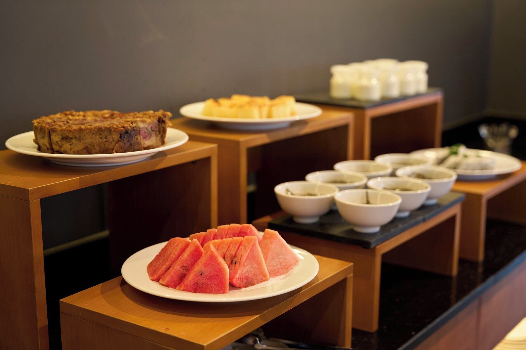 Un bufé con diversos platos, incluyendo una bandeja de frutas, un postre y varias cazuelas de sopa.