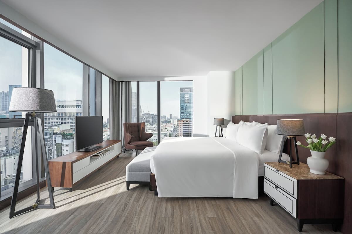 A modern hotel room with a large bed, a desk, a chair, and a TV.