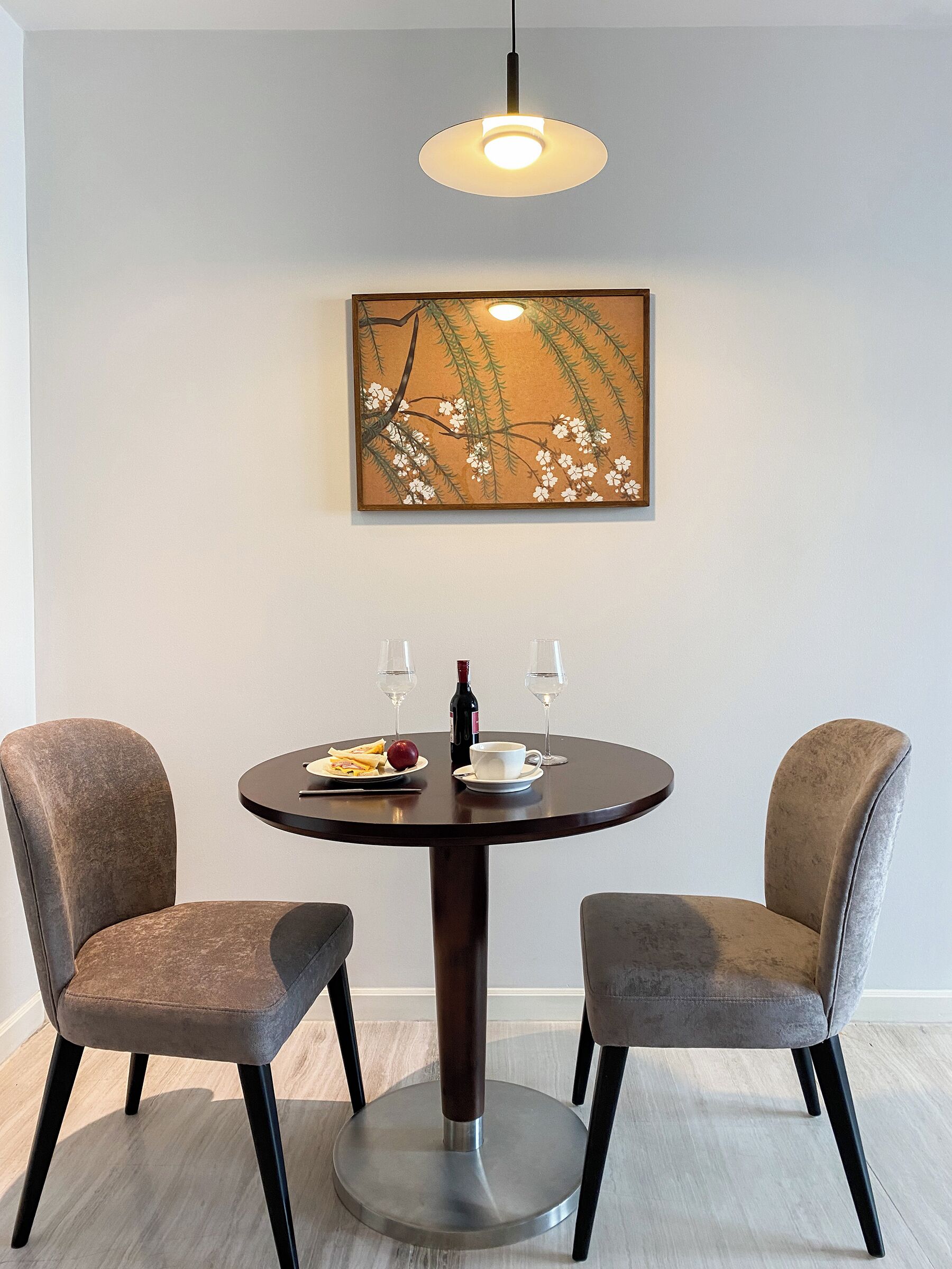 A dining table with two chairs, a painting above, and a bottle and glasses on the table.