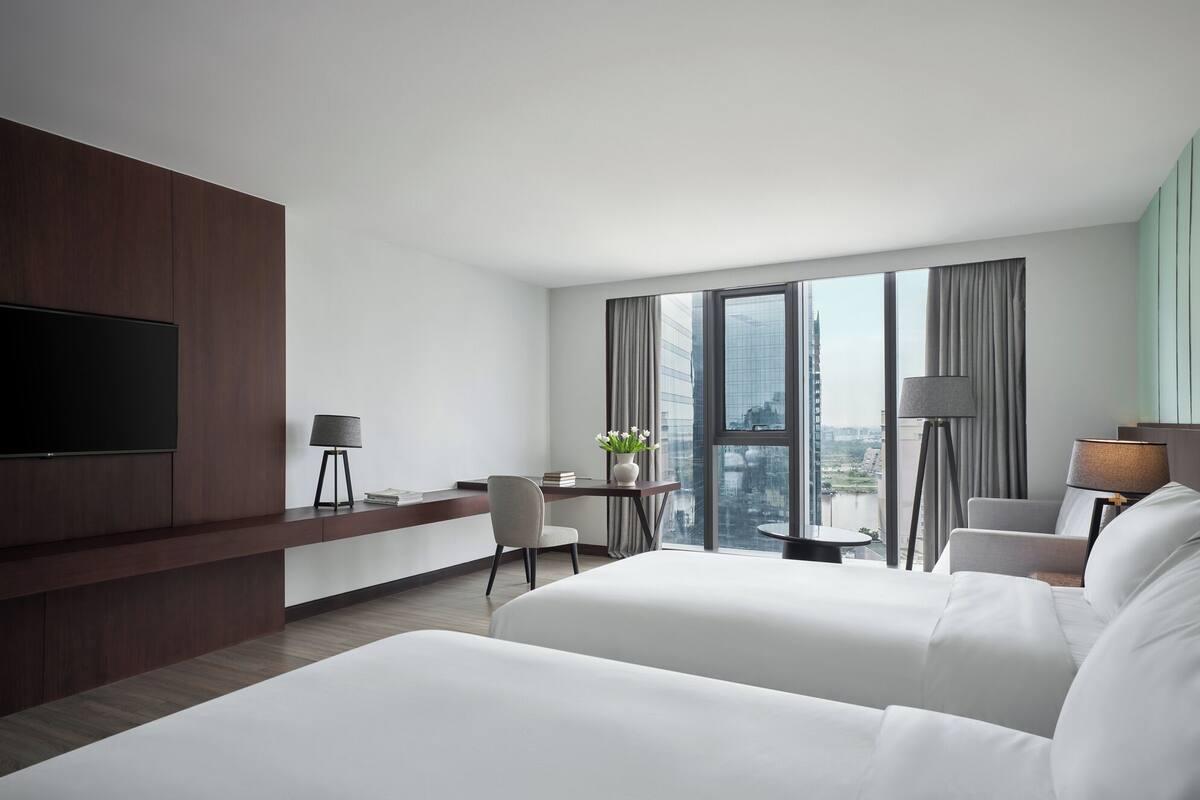 A hotel room with a large bed, a desk, a TV, and a view of the city.