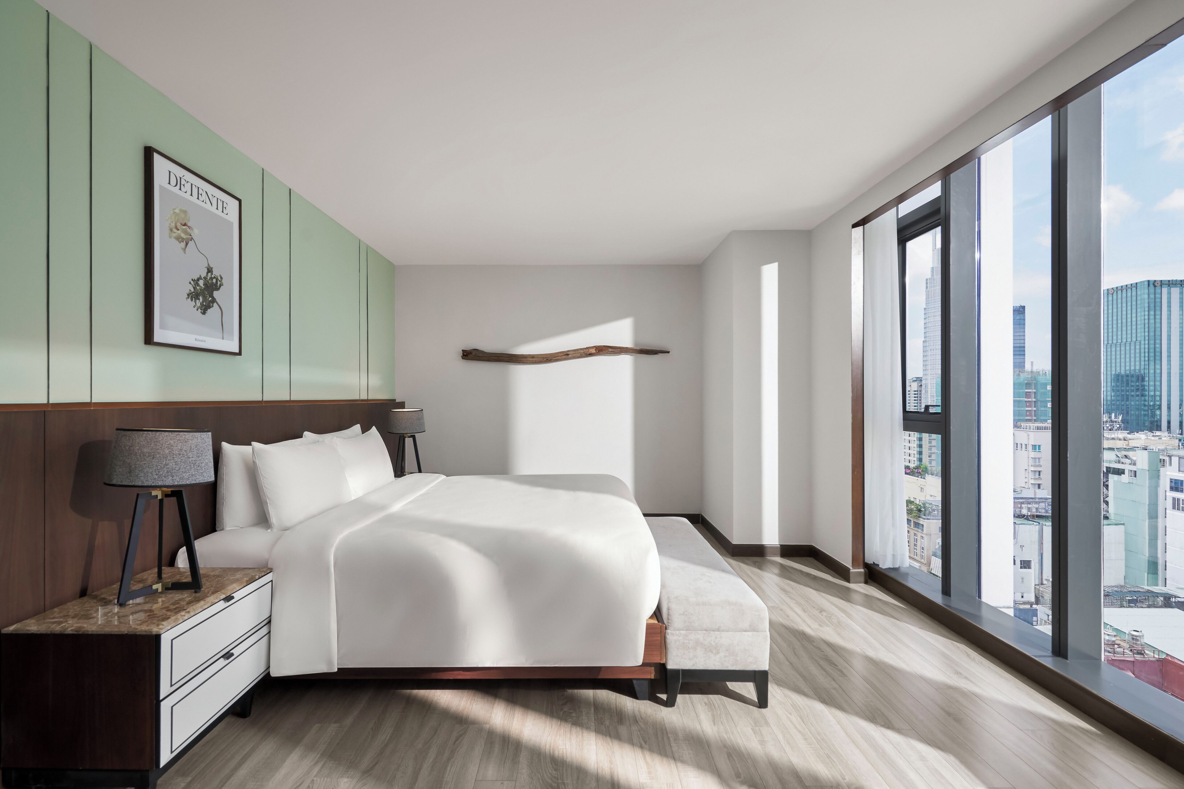 A modern bedroom with a large bed, a nightstand, a bench, and a city view through large windows.