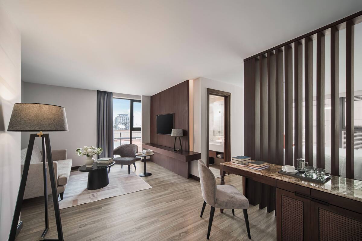 A modern hotel room with a desk, seating area, and large windows offering a city view.