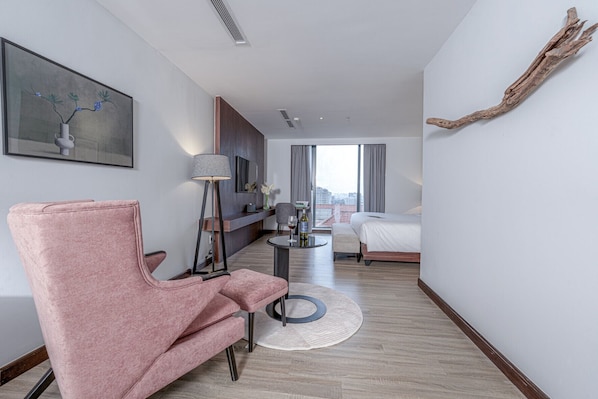 A modern hotel room with a pink armchair, a round table with a lamp, a bed, and a view of the city through large windows. - Signature by M Village Lê Thánh Tôn, a brand of Modern Village Lifestyle (Ho Chi Minh City)