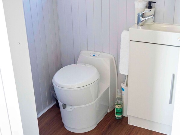 A small bathroom with a white toilet, a white sink, and a bottle of green cleaning product.