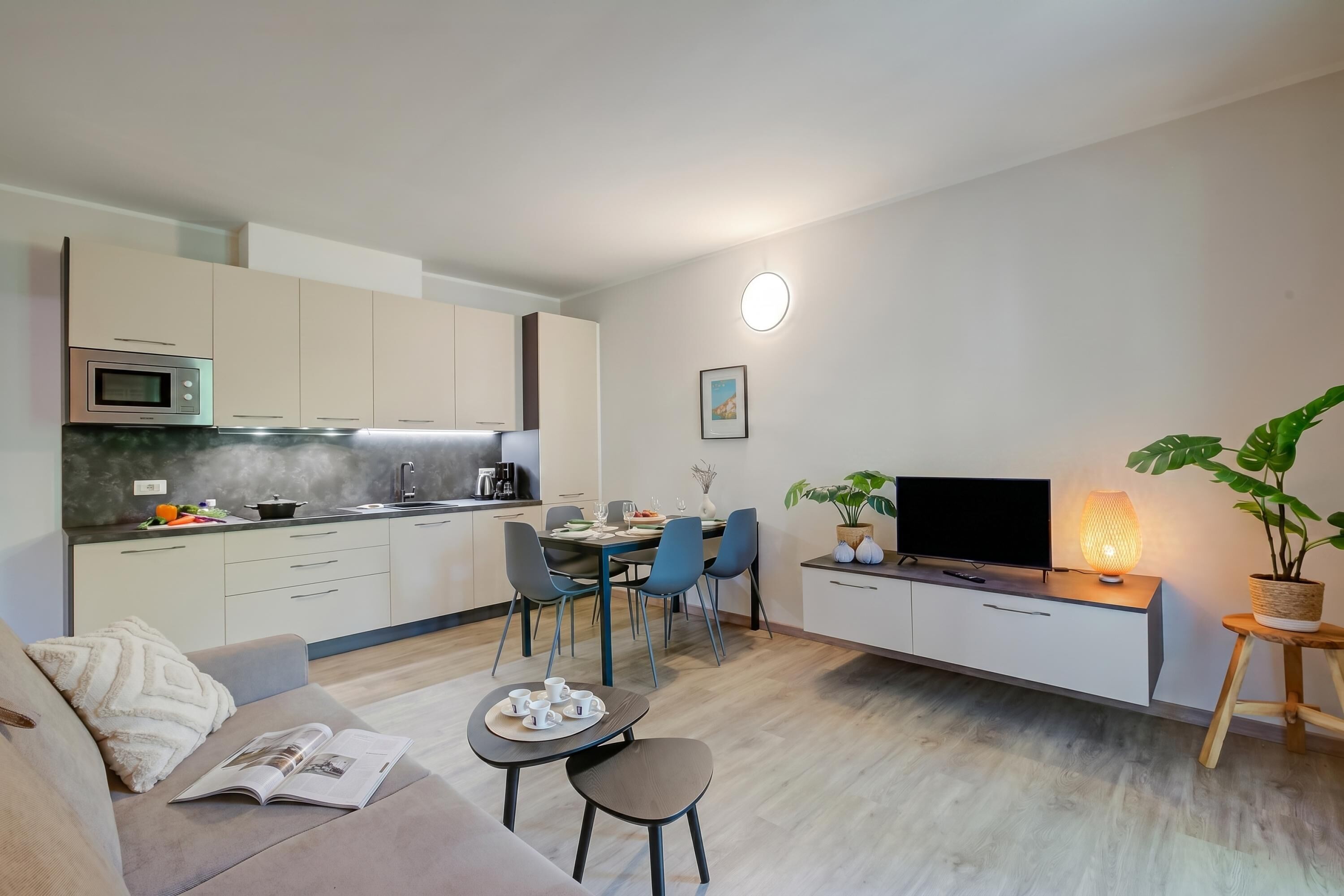 Une cuisine moderne équipée d’un four à micro-ondes, d’une table à manger, de chaises et d’un téléviseur posé sur un meuble.