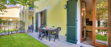 Une terrasse avec une table et des chaises, une porte donnant sur la cuisine et un petit jardin.