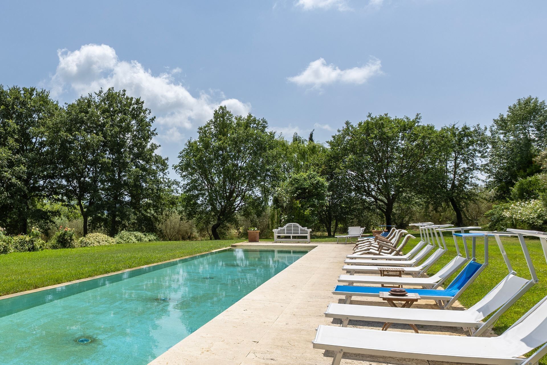 Un área junto a la piscina con sillones de descanso y un pequeño pabellón blanco.
