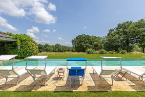A poolside area with lounge chairs and a table, surrounded by greenery and trees. - Villa Federica 17 by Anita Villas (Manciano)