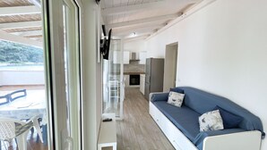 Un salon moderne avec un canapé, une petite table et un coin cuisine visible à travers une porte ouverte.
