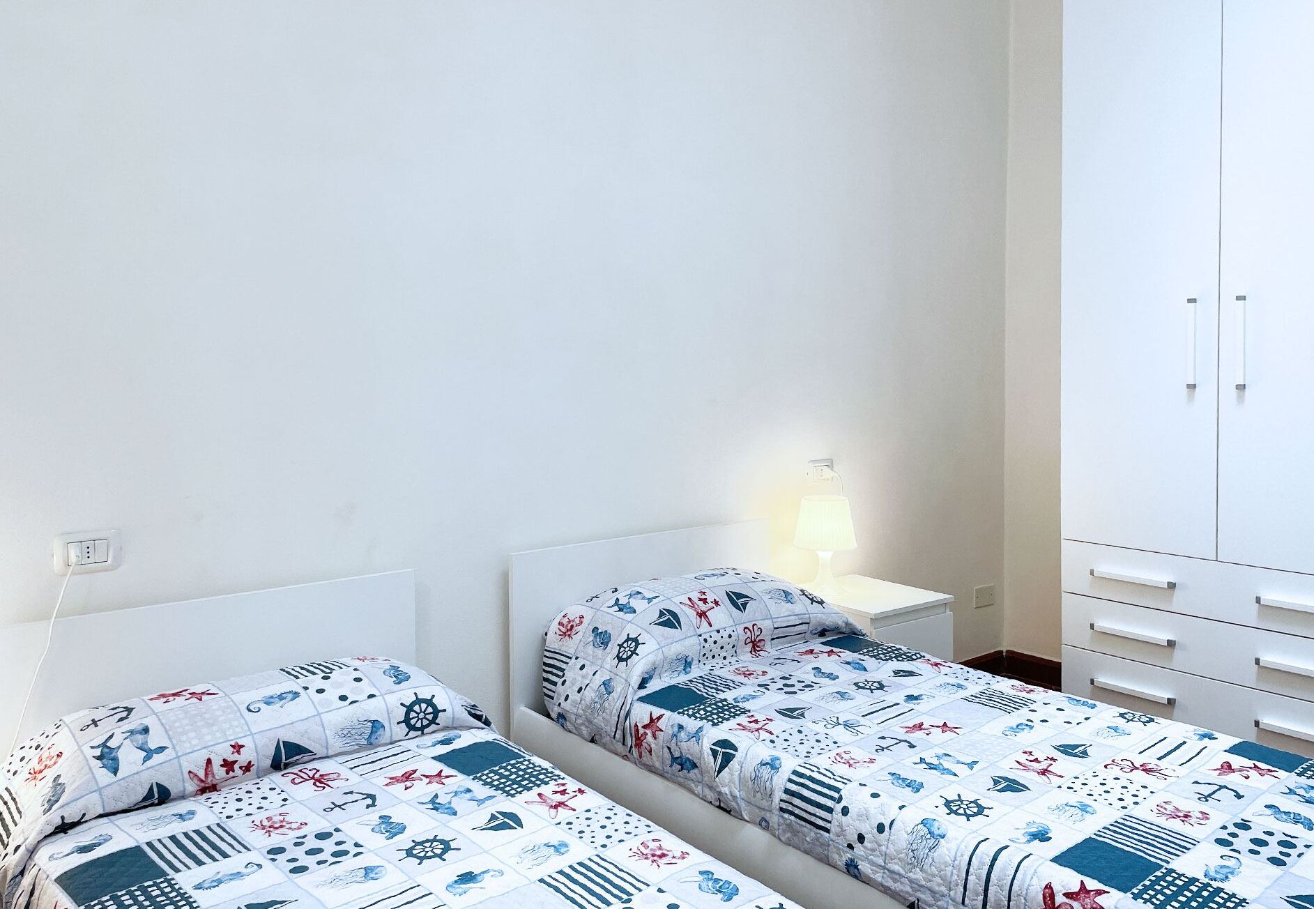 Une chambre avec deux lits, une table de chevet avec une lampe et une armoire blanche.