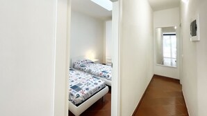 Un couloir étroit avec deux lits, chacun recouvert d’une courtepointe à motifs, mène à une pièce dotée d’une fenêtre.