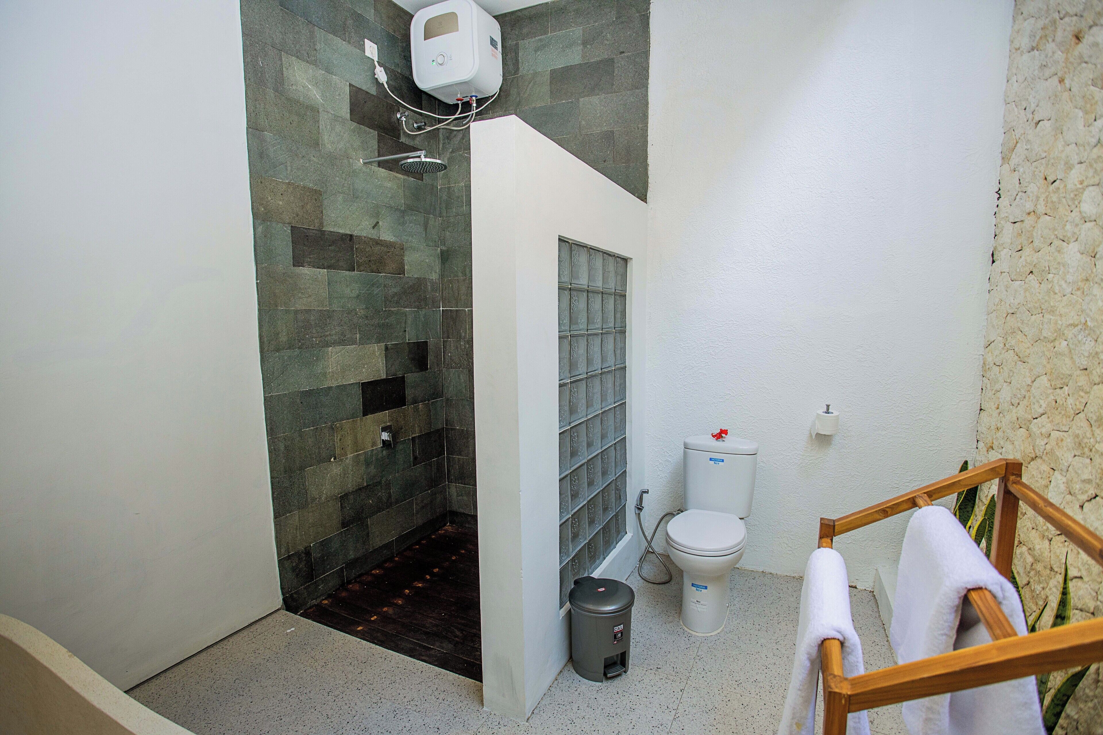 A bathroom with a shower, toilet, and a wooden chair with a towel.