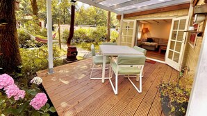 Un patio couvert avec une table et des chaises, une terrasse en bois et un jardin agrémenté d’hortensias roses.